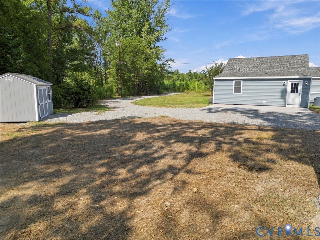 Exterior featuring grey vinyl siding, shingled roofing, a gravel driveway, and a detached storage shed