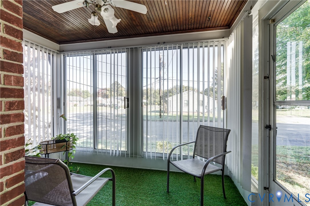 Enclosed porch featuring a wood-plank ceiling, exposed brick wall, floor-to-ceiling glass windows, vertical blinds, and an overhead ceiling fan with light fixture