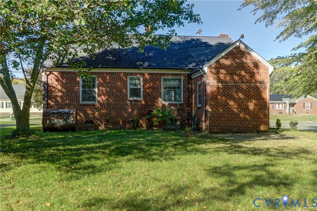 Exterior red brick facade featuring a dark shingle roof, multi-pane windows, and a mature tree-lined lot