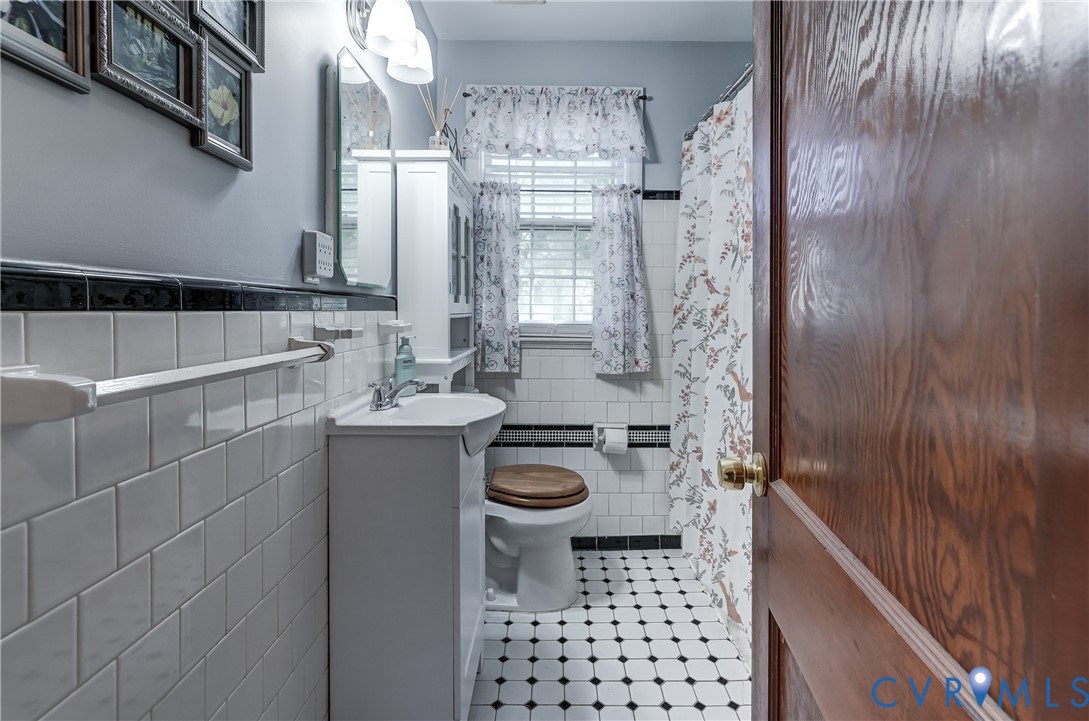 Bathroom featuring white subway wall tile with black decorative trim, pedestal sink, and black-and-white hex tile flooring