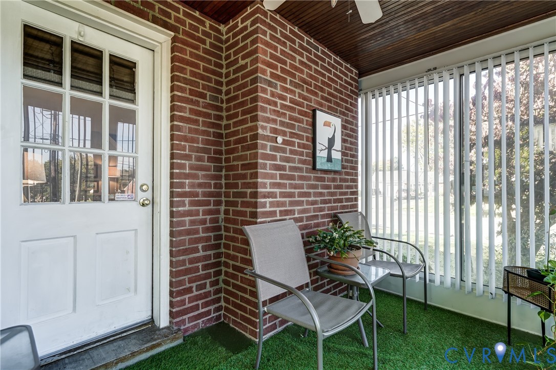 Enclosed porch featuring exposed brick wall, nine-lite glass panel door, wood-paneled ceiling, and vertical window blinds