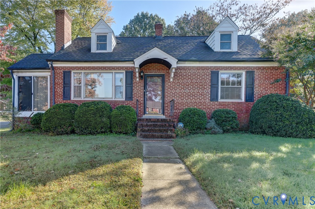 Brick exterior featuring dual dormer windows, a central arched entry portico, and a chimney stack