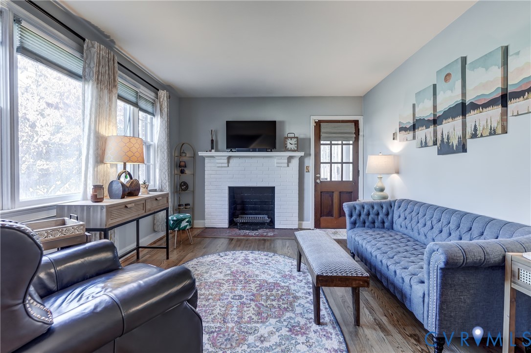 Painted brick fireplace with a mantel, wood-finish flooring, multi-pane glass door, and large windows