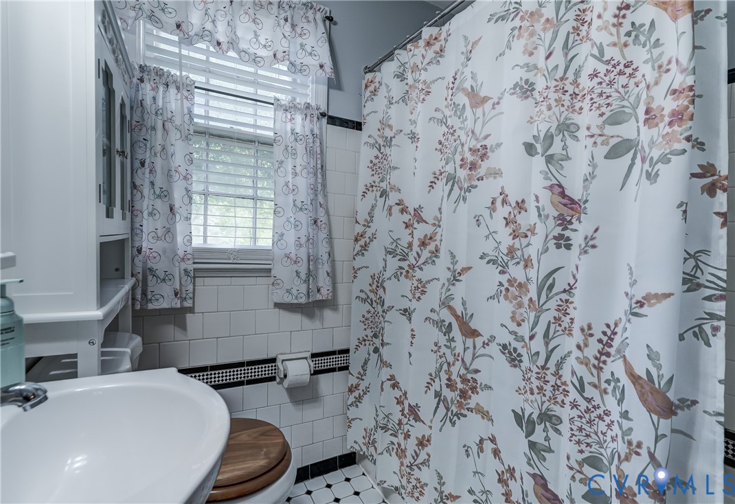 Bathroom featuring white subway wall tile with black accent detailing, built-in white cabinetry, a porcelain pedestal sink, and black-and-white mosaic tile flooring