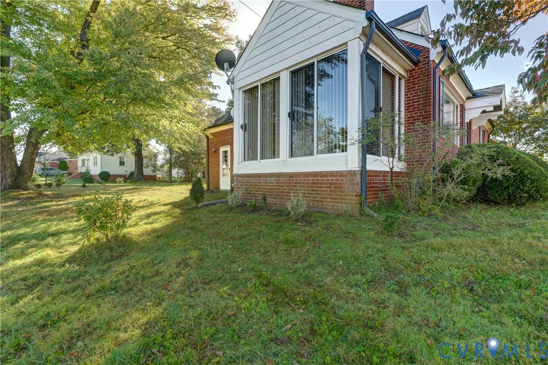 Brick and white siding exterior featuring a multi-windowed sunroom and mature landscaping