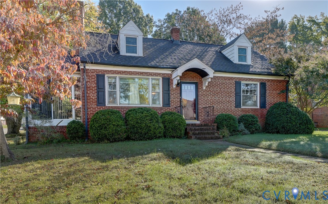 Brick exterior featuring two dormer windows, an arched covered entryway, shuttered multi-pane windows, and a shingled roof