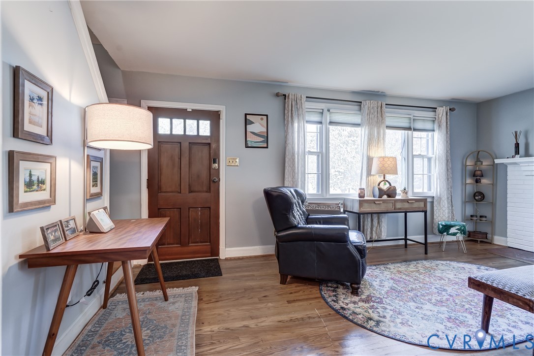 Living area featuring wood-finish flooring, a multi-paneled wood entry door with glass transom accents, multi-pane windows, and a white brick fireplace surround