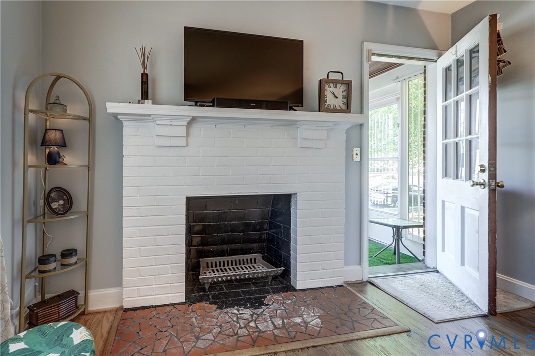 Painted white brick fireplace featuring a mantel shelf and a masonry hearth with a geometric tile inlay, wood-finish flooring, and a multi-pane glass entry door