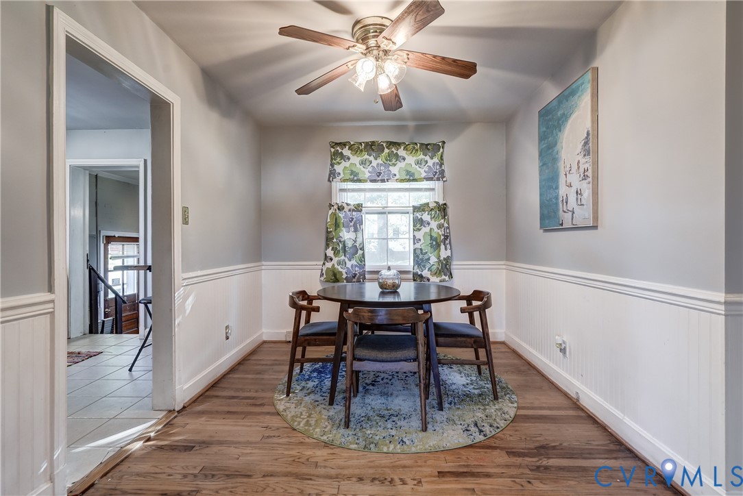 Wood-finish flooring, chair rail molding, wainscoting, and a multi-light ceiling fan
