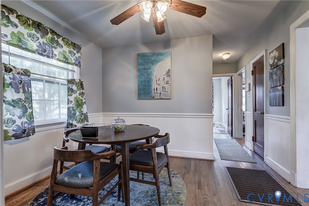 Wood-finish flooring, white wainscoting, multi-pane windows, and a ceiling-mounted light fixture with a fan