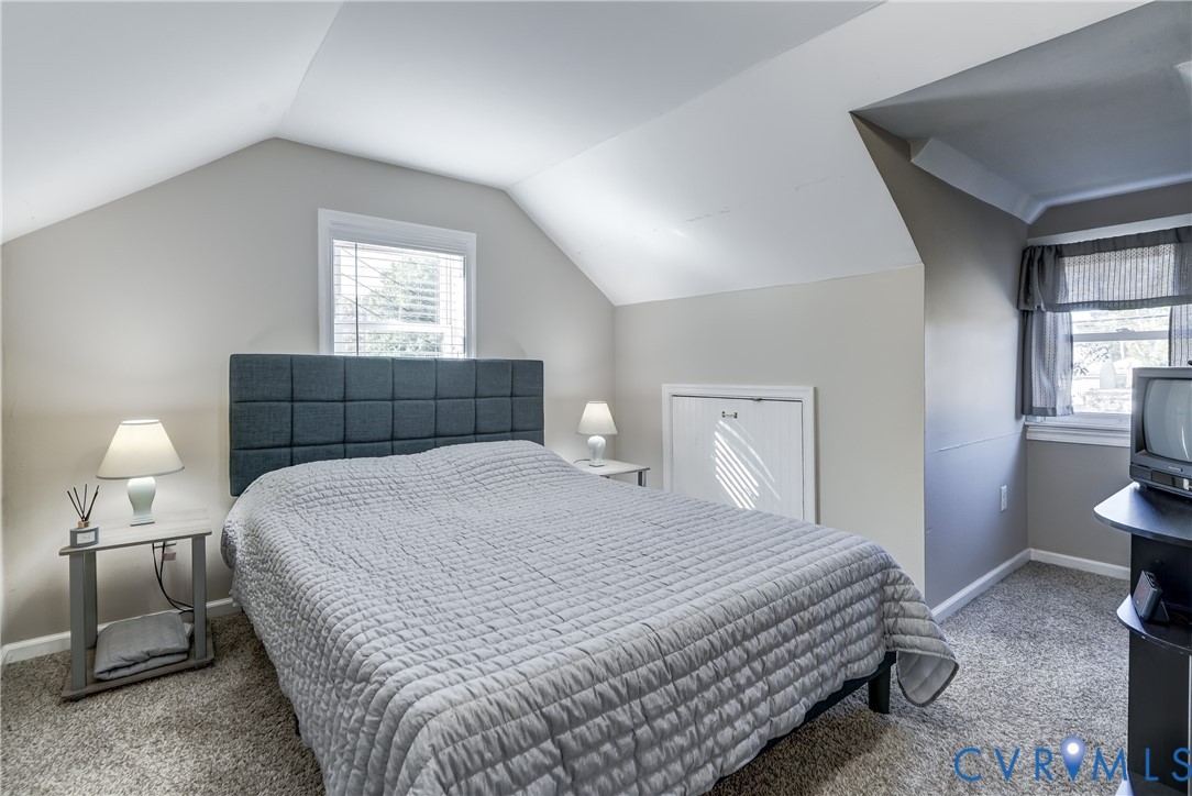 Vaulted ceilings with dormer window, neutral wall palette, and built-in knee-wall storage access