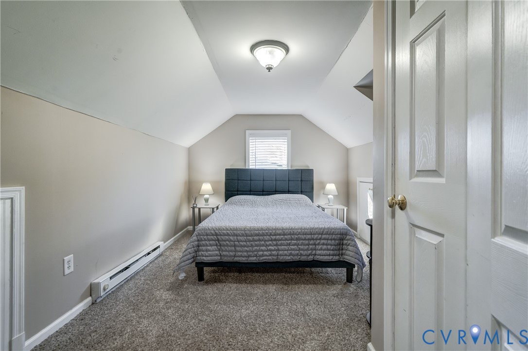 Room featuring carpeted flooring, vaulted ceilings, and a central window with sloped architectural walls