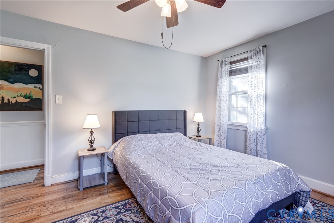 Wood-finish flooring, neutral wall tones, multi-light ceiling fan, and window featuring light-filtering treatments