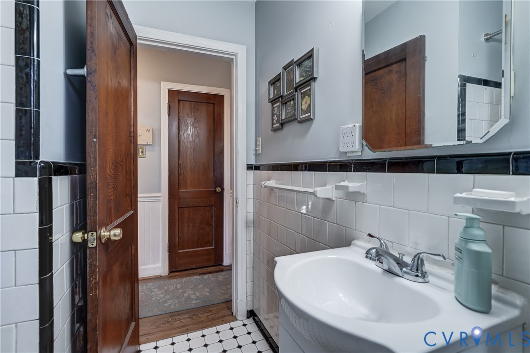 Bathroom featuring white wall tile with black trim, pedestal sink with dual-handle faucet, checkered tile flooring, and solid wood-finish doors