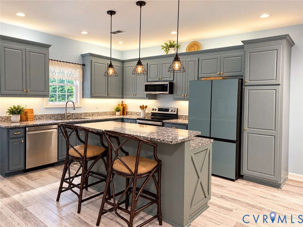 Kitchen featuring custom blue-gray cabinetry, stone-surface countertops, central island, stainless steel appliances, and hanging cage-style pendant lighting