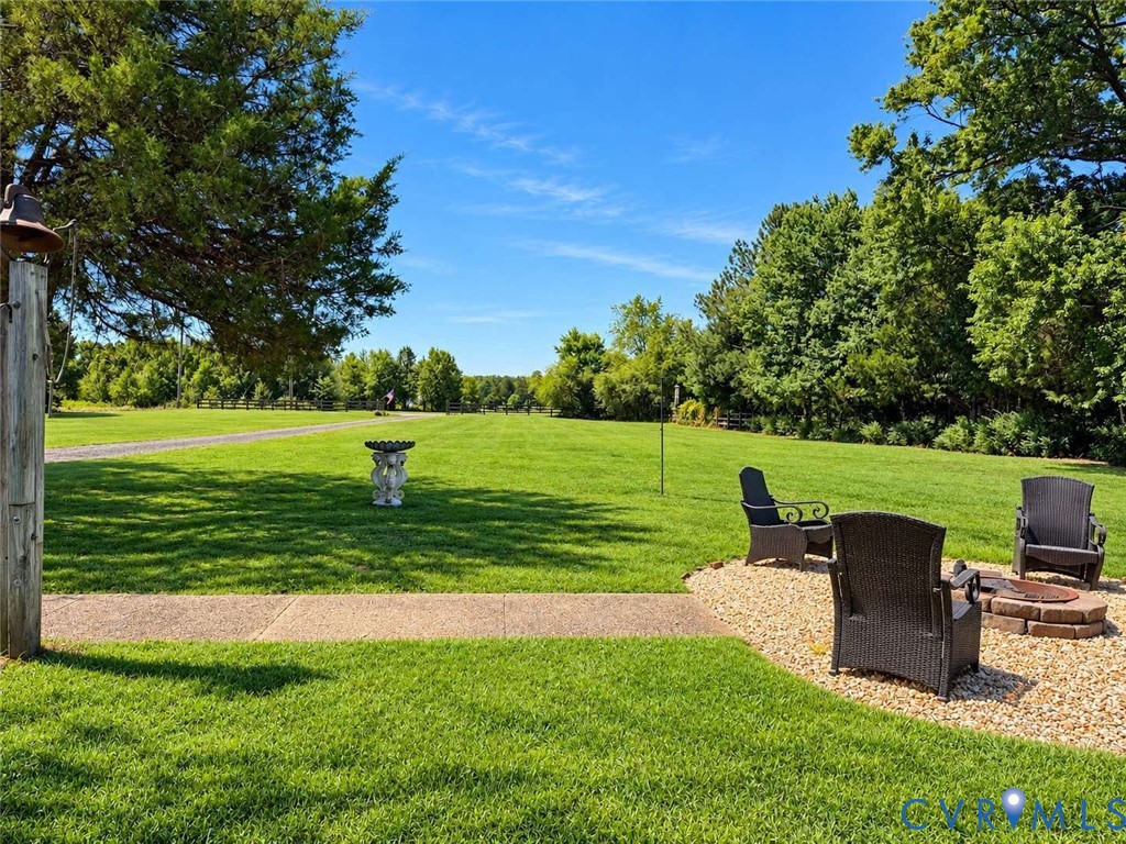 Expansive grounds featuring a manicured lawn, stone-surrounded fire pit, concrete pathway, and mature tree canopy