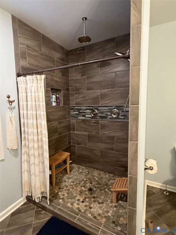 Walk-in shower featuring large-format wall tile, a recessed niche, a decorative mosaic tile accent border, a ceiling-mounted rainfall showerhead, and a stone pebble floor