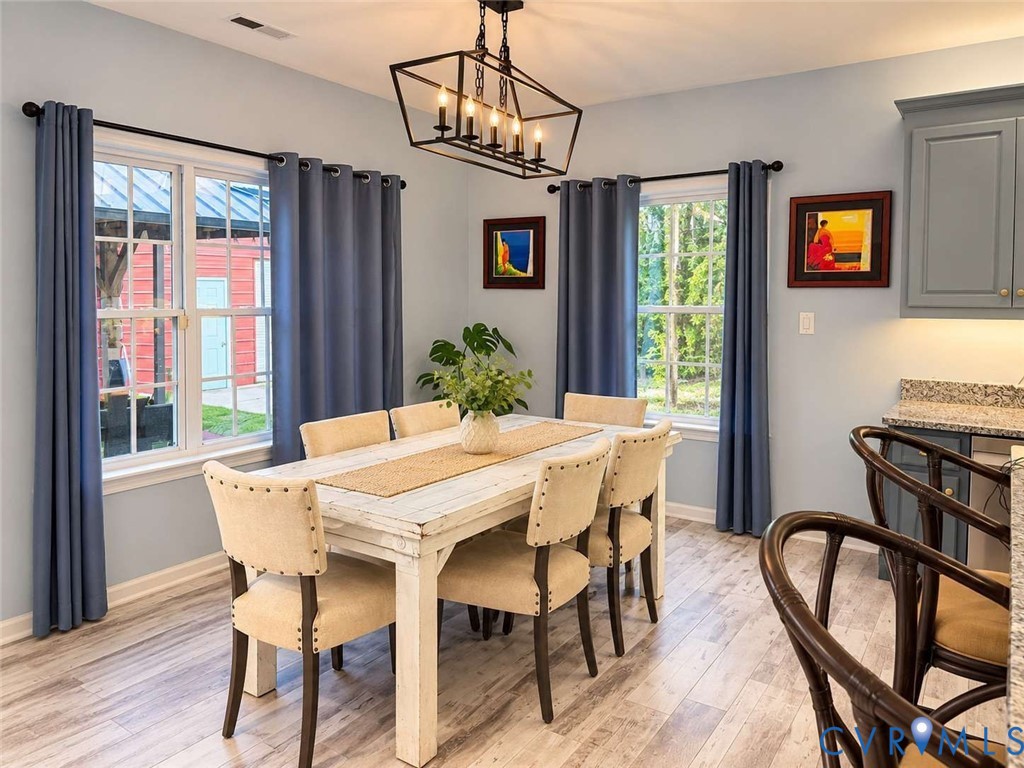 Dining space featuring wood-finish flooring, a geometric metal chandelier, multi-pane windows, and light-toned cabinetry with stone-finish countertops