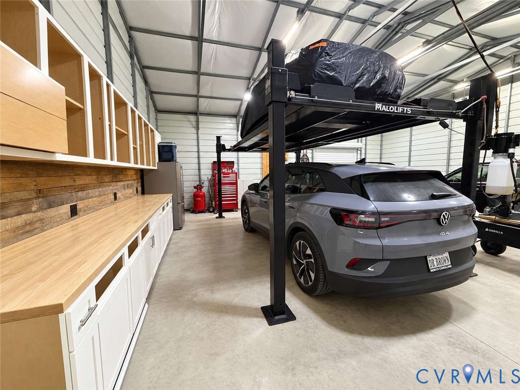 Workshop garage featuring high-clearance metal construction, integrated automotive lift, expansive wood-topped built-in cabinetry, and textured wood panel wall accents