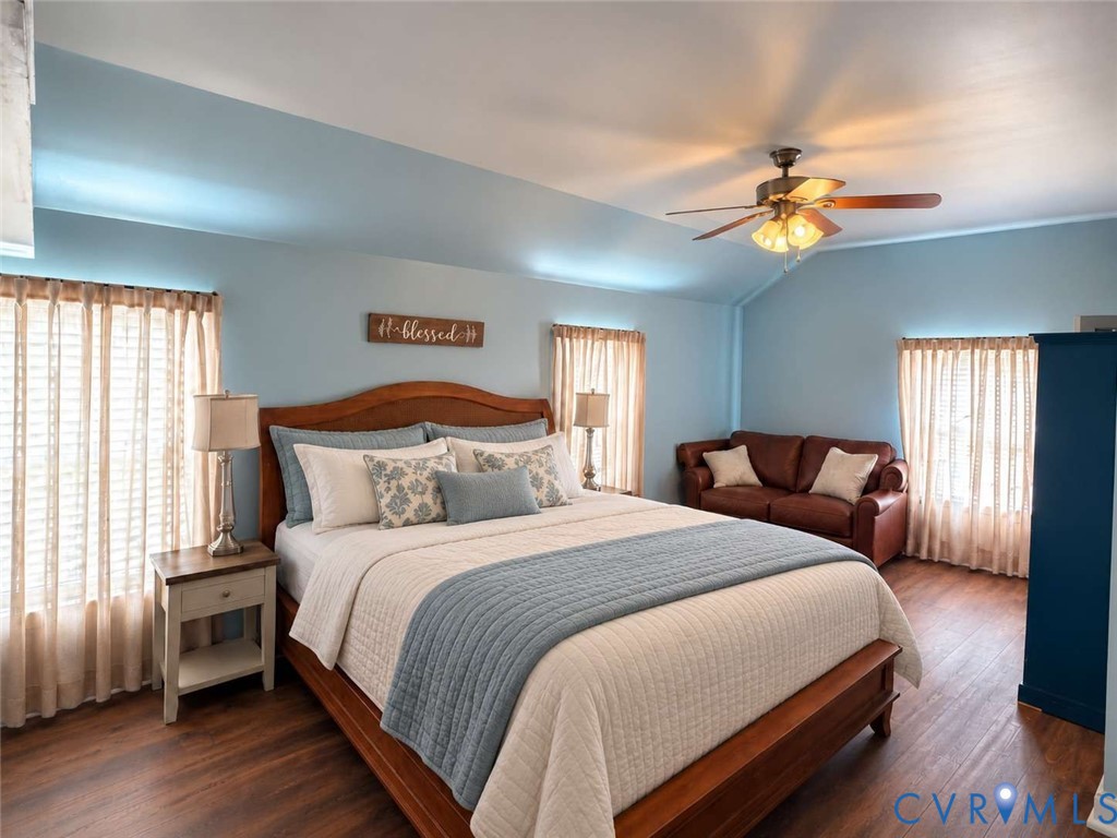 Vaulted ceiling, wood-finish flooring, and multiple windows with fixed window treatments