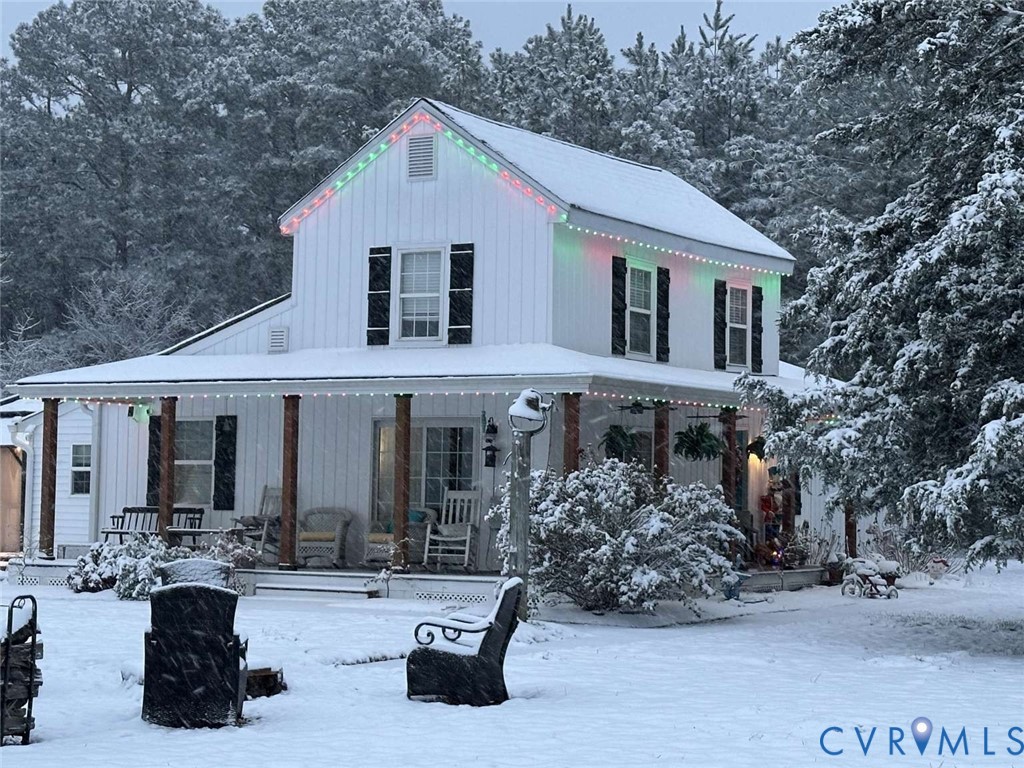 Two-story farmhouse exterior featuring white board-and-batten siding, black shutters, a wrap-around covered porch with wood-finished columns, and a peaked roofline