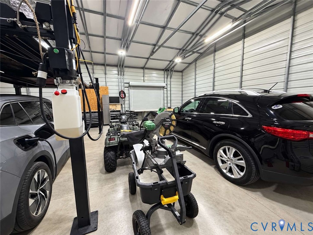 Detached workshop featuring corrugated metal walls, concrete flooring, high-clearance overhead door, and LED tube lighting