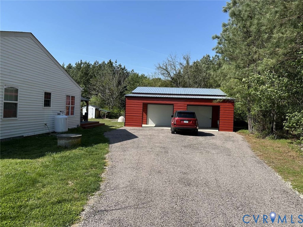 Detached two-car garage with metal roofing, red horizontal siding, and gravel driveway