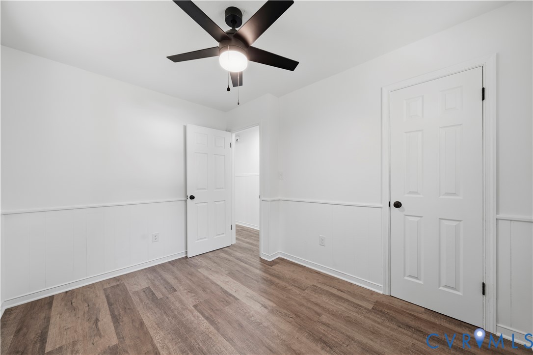Room featuring wood-finish flooring, wainscoting, matte black door hardware, and a ceiling-mounted light fixture with a fan