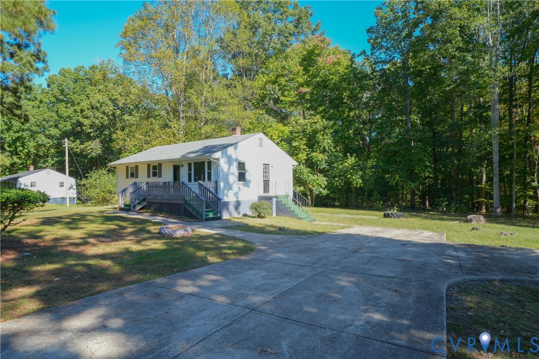 Exterior featuring white siding, a concrete driveway, raised wood-finish decking, and mature trees on a lot
