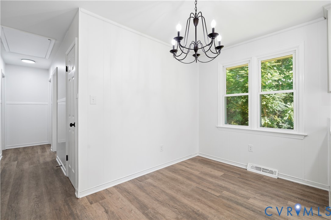 Wood-finish flooring, white paneling, dual-pane window, and an intricate dark metal chandelier