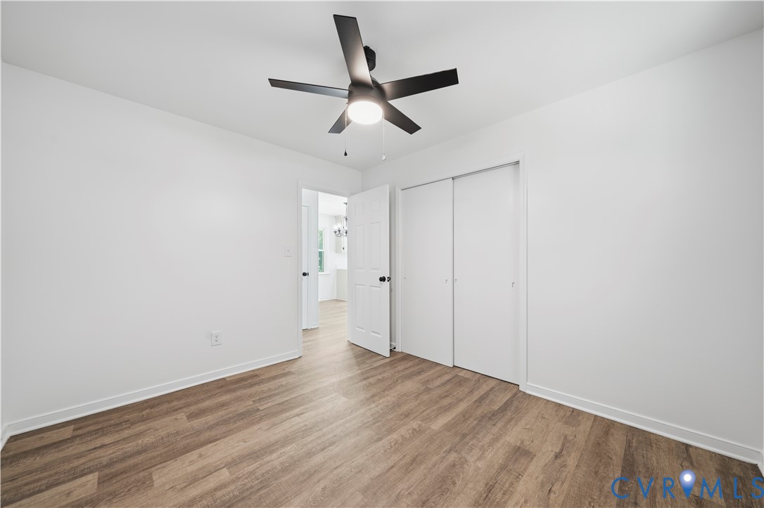 Room featuring wood-finish flooring, a matte black multi-blade ceiling fan with integrated lighting, and a closet with sliding doors