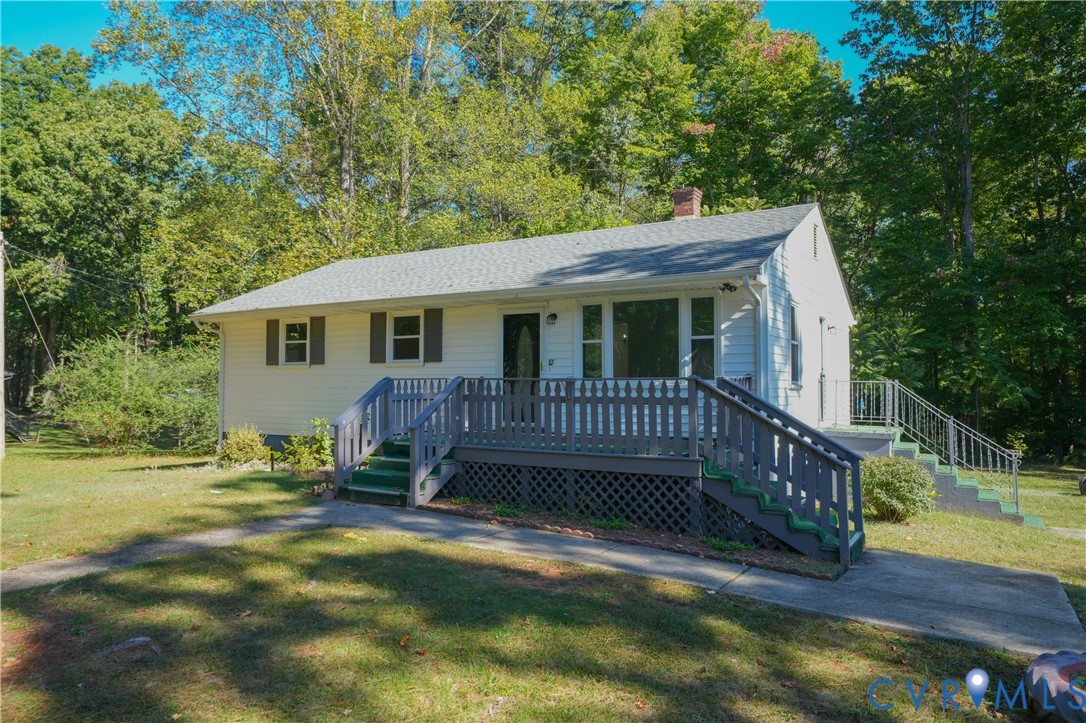 Single-story exterior with light siding, gable roofline, elevated wood-finish deck featuring lattice skirting, and concrete walkway Single-story exterior with light siding, gable roofline, elevated wood-finish deck featuring lattice skirting, and concrete walkway
