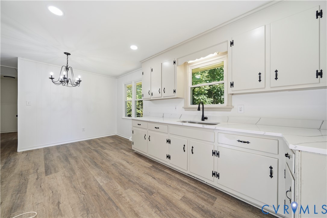 Kitchen featuring cabinetry with matte black hardware, stone-finish countertops, an undermount sink with a matte black faucet, wood-finish flooring, and a multi-arm chandelier