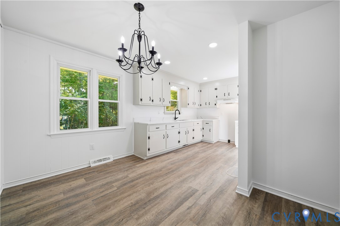 Kitchen featuring wood-finish flooring, white cabinetry, a matte black faucet, and a six-light iron chandelier