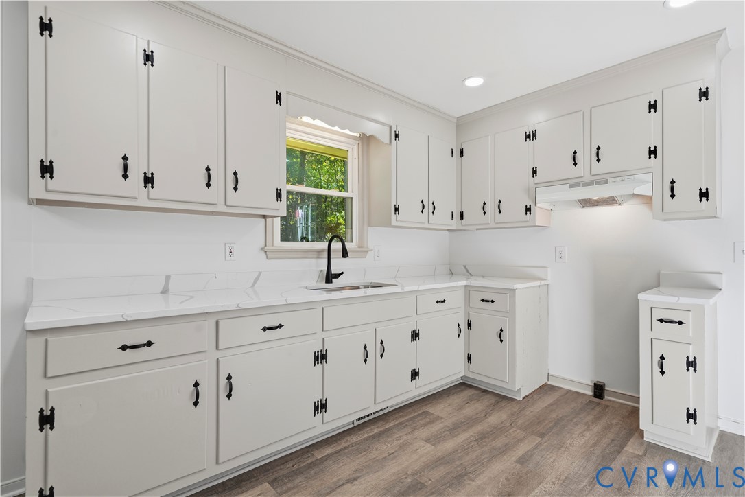 Kitchen featuring light-toned cabinetry with matte black hardware, stone-finish countertops, an undermount sink with a high-arch faucet, recessed lighting, and wood-finish flooring