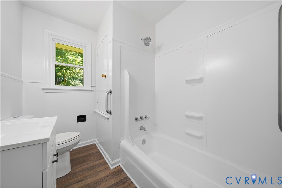 Bathroom featuring wood-finish flooring, white vanity with integrated sink, composite tub surround, and fixed metal grab bar