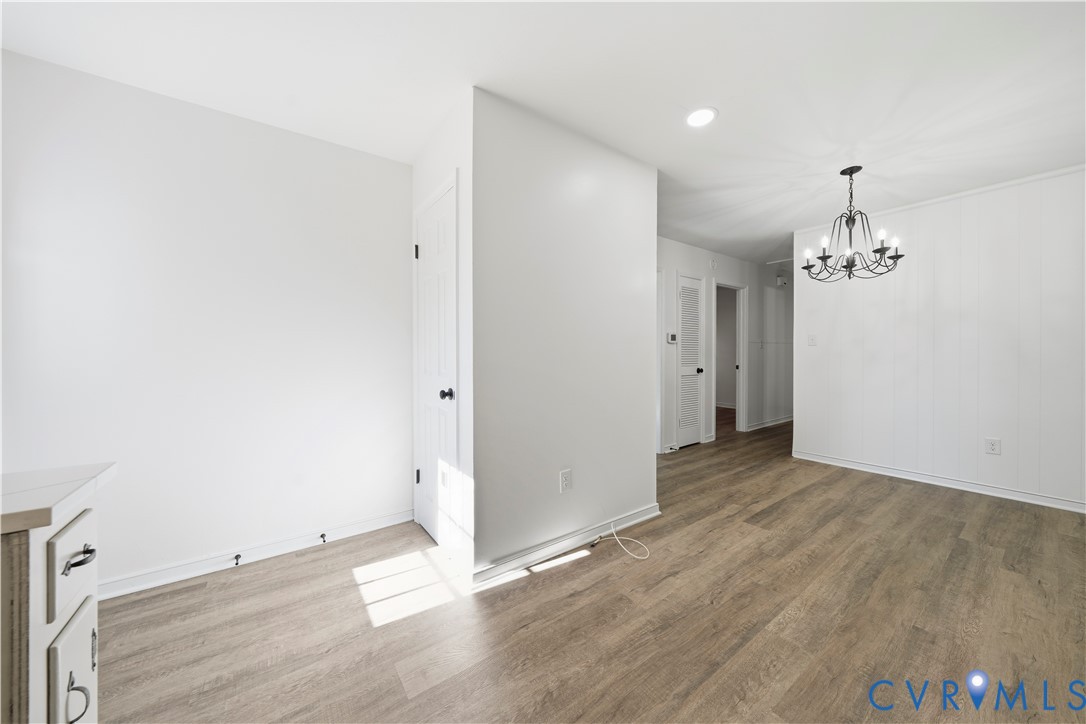 Interior space featuring wood-finish flooring, white panel walls, and a multi-arm chandelier