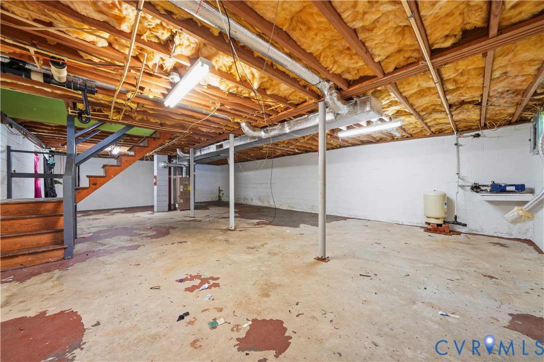 Unfinished basement area featuring painted masonry walls, exposed ceiling joists with insulation, concrete flooring, metal support columns, and overhead strip lighting