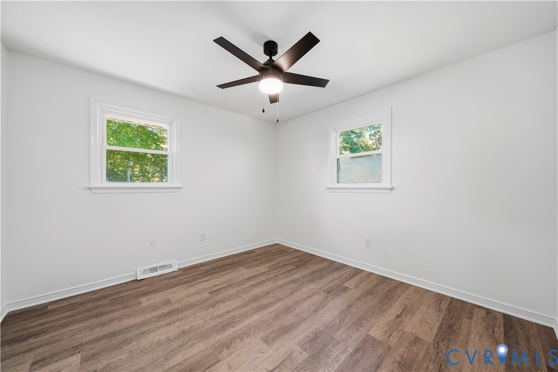 Room featuring wood-finish flooring, dual windows, and a central ceiling fan with an integrated light fixture