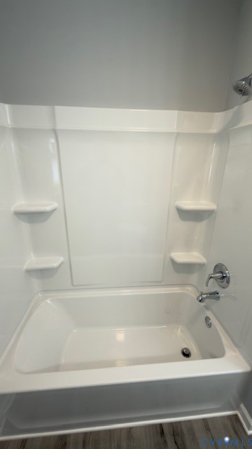 Bathtub with a white acrylic surround, built-in shelving, chrome faucet hardware, and a fixed shower head