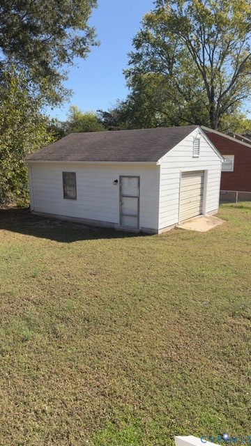 Detached garage featuring white horizontal siding, a gabled roof with shingles, an exterior pedestrian door, and a roll-up garage door