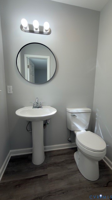 Pedestal sink with a polished chrome faucet, round wall-mounted mirror with a dark frame, three-light vanity fixture, and wood-finish flooring