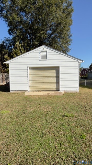 Detached garage featuring white horizontal siding, a roll-up door, gable roof, and concrete foundation