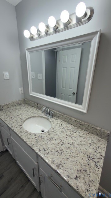 Vanity featuring stone-finish countertop, integrated undermount sink, white cabinetry with silver-tone hardware, framed mirror, and multi-bulb polished nickel light fixture