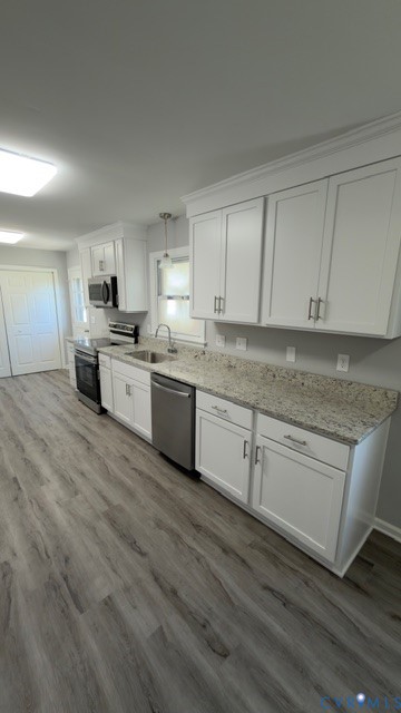 Kitchen featuring white shaker-style cabinetry, neutral stone-finish countertops, stainless steel appliances, and wood-finish flooring