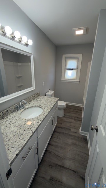 Bathroom featuring white cabinetry, a stone-finish countertop with an integrated oval sink, wood-finish flooring, and a multi-bulb vanity light fixture