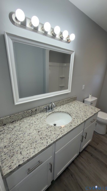 White vanity with speckled stone-patterned countertop, integrated white sink, framed mirror, five-bulb light fixture, and wood-finish flooring