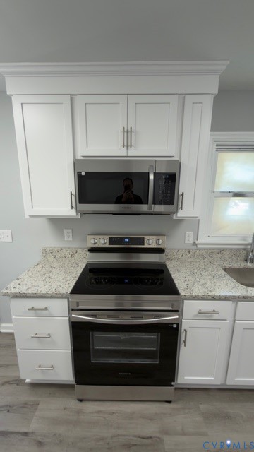 Kitchen featuring white shaker-style cabinetry with crown molding, stone-patterned countertops, stainless steel electric range, built-in stainless steel microwave, and wood-finish flooring