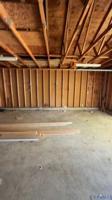 Garage space featuring exposed wood-stud walls, concrete flooring, and an open-rafter ceiling with surface-mounted lighting