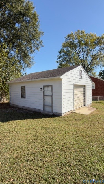 Detached garage featuring white horizontal siding, a pitched asphalt shingle roof, a roll-up garage door, and a side-entry door